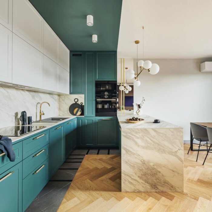Luxury modern and vintage turquoise interior. Marble kitchen island with wooden chockers. Brown wooden table with metalic tray and metalic gold vase with white decorations.